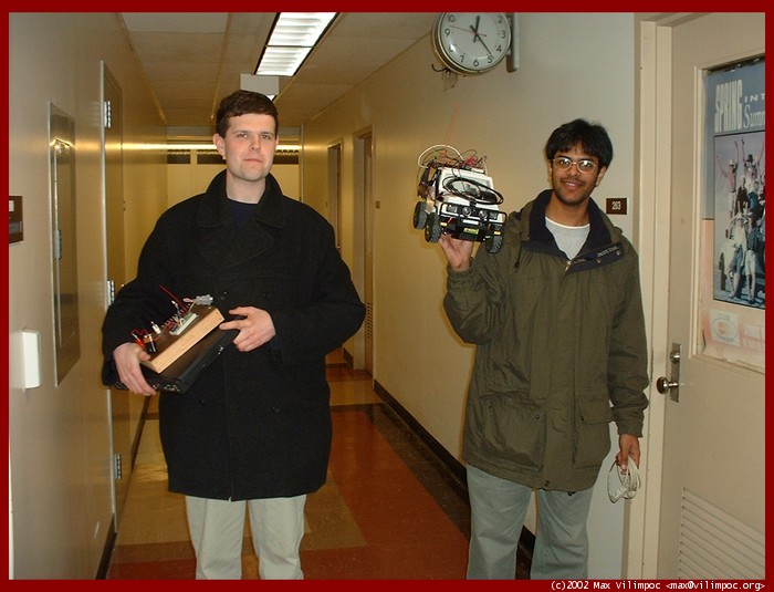 Pat and Aravind walking down the Caldwell Labs hall, holding the remote control board and car