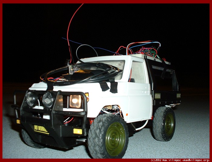 A close up of the remote control car with all sorts of wires hanging off
