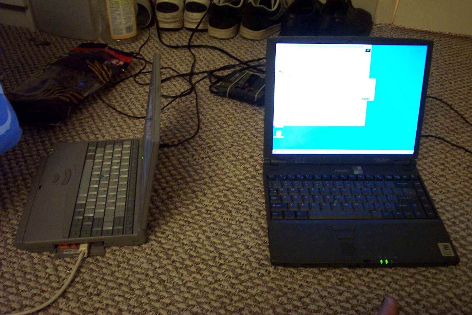 Two laptops, both powered on and running Windows, sitting on carpet