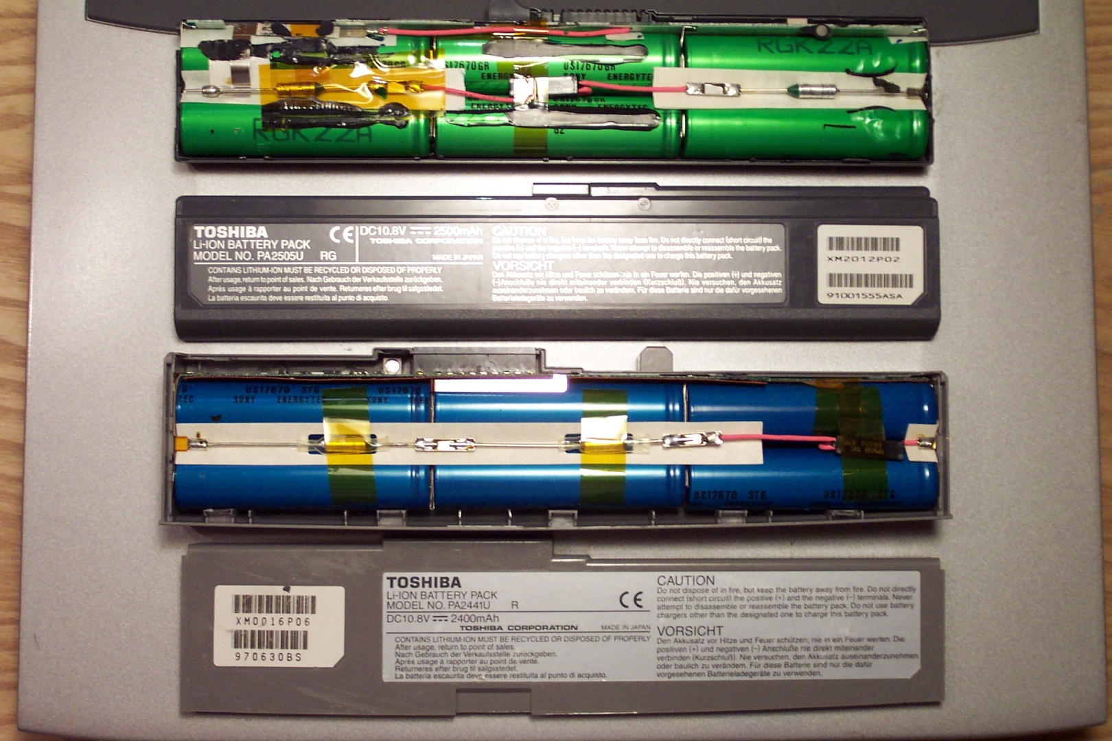 Two laptop batteries, with part of the casing removed. Each pack has six 18650 cells, one pack has green cells, one pack has blue cells.