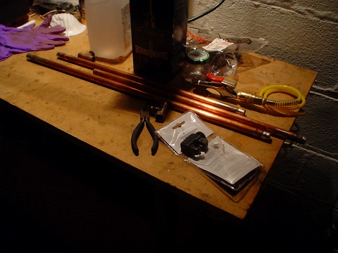 3 long pieces of copper tubing on the workbench, a pair of pliers, and a copper pipe cutter