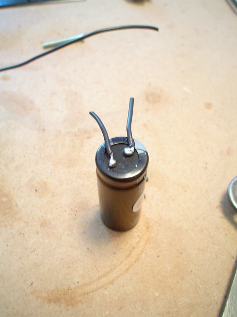 A large capacitor with two pieces of black signal signal wires soldered on